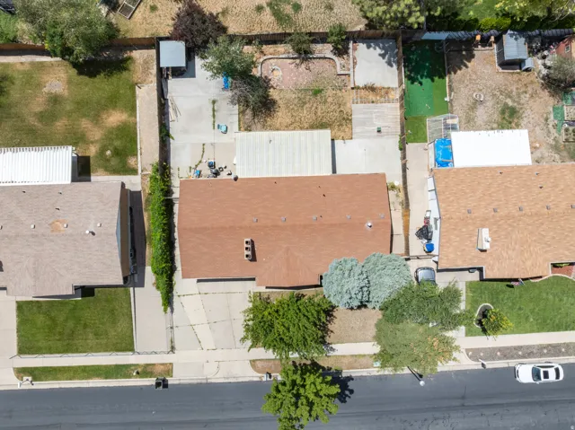 Overhead view showcasing a property with a brown shingle roof, mature front yard trees, paved driveway, and an expansive concrete patio in the rear