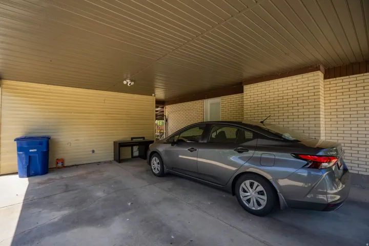 Covered parking area with concrete flooring, light brick wall, and beige horizontal siding
