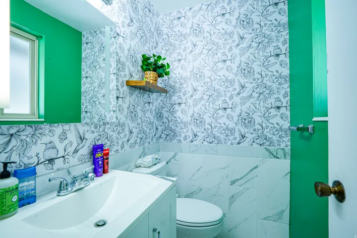 Bathroom featuring a white vanity with integrated sink, chrome faucet, and patterned wallpaper