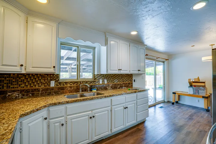 Kitchen featuring white cabinetry, granite-finish countertops, mosaic tile backsplash, stainless steel double basin sink, and recessed lighting