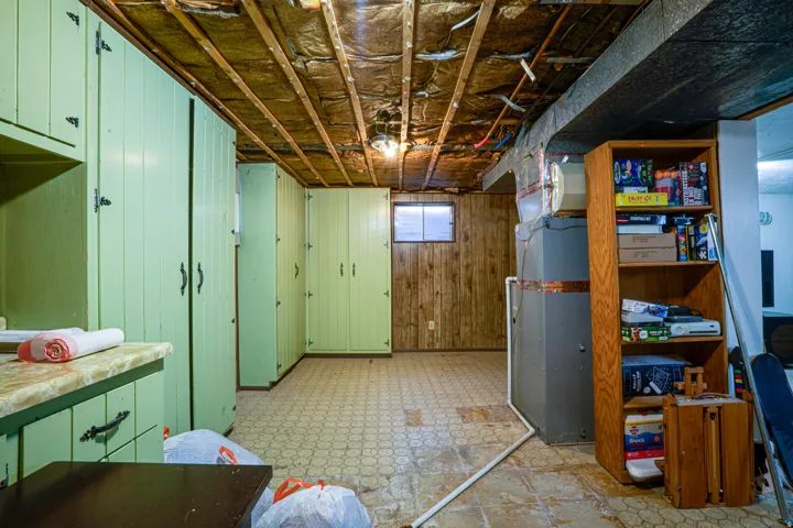Basement utility area featuring extensive built-in cabinetry, wood paneling, and an exposed ceiling