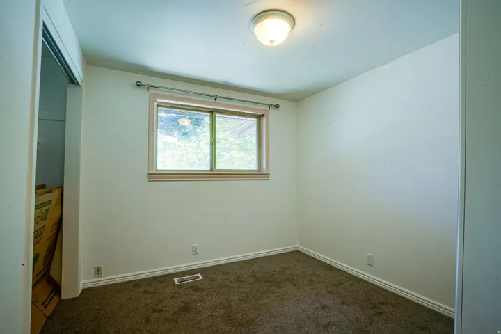 Carpeted room featuring a window with a wood-finish trim, a flush-mount ceiling light fixture, and white baseboards