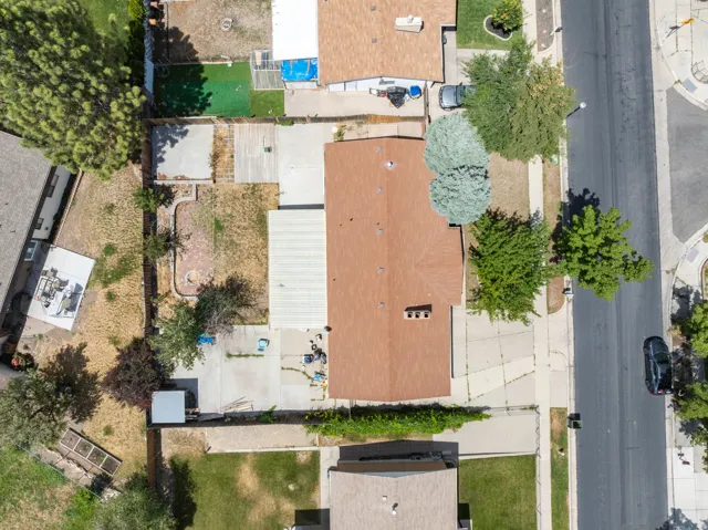 Single-story residence featuring a brown shingle roof, a front yard with mature trees, and an extensive paved driveway