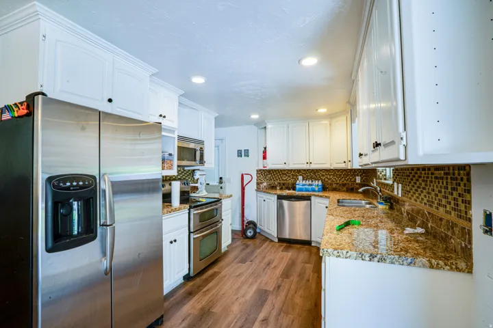 Kitchen featuring white cabinetry, integrated stainless steel appliances, granite countertops, a mosaic tile backsplash, and wood-finish flooring