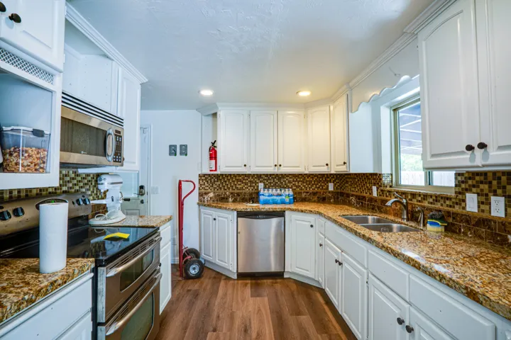 Bright kitchen featuring white cabinetry, granite-finish countertops, stainless steel appliances, a mosaic tile backsplash, and wood-finish flooring