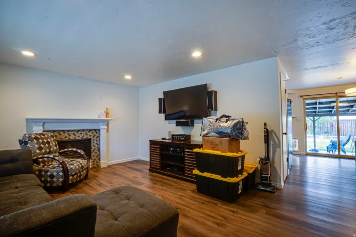 Living area featuring wood-finish flooring, a fireplace with a white mantel and mosaic tile surround, recessed lighting, and white walls