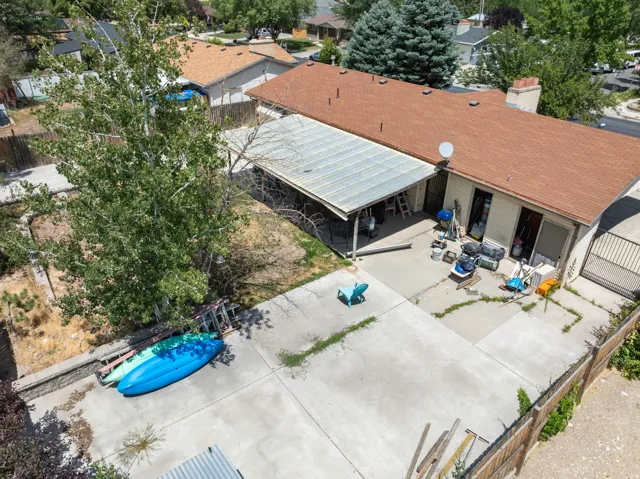 Rear exterior featuring a covered patio, concrete patio, tan siding, and a brown shingle roof