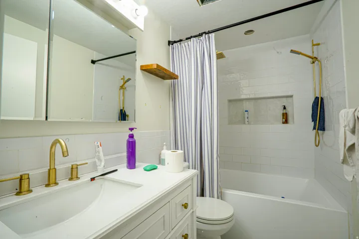 Bathroom featuring a white vanity with gold-tone hardware, a gold-tone sink faucet, a built-in bathtub, and white subway tile shower surround with an integrated niche