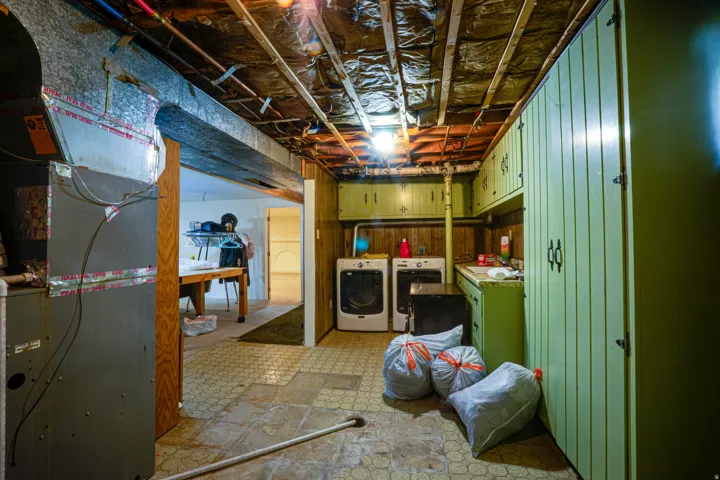Basement utility area featuring a washer and dryer, built-in cabinetry, overhead lighting, and exposed ceiling joists