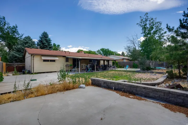 Expansive backyard featuring a covered patio, a concrete patio area, a raised garden bed, and mature trees