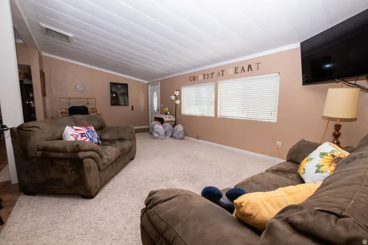Carpeted living area featuring a vaulted ceiling with white paneling and a wall-mounted flat-screen television