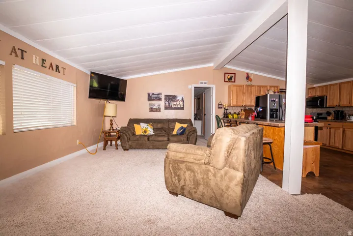 Living area with vaulted ceilings, recessed window with blinds, and light-toned carpeting