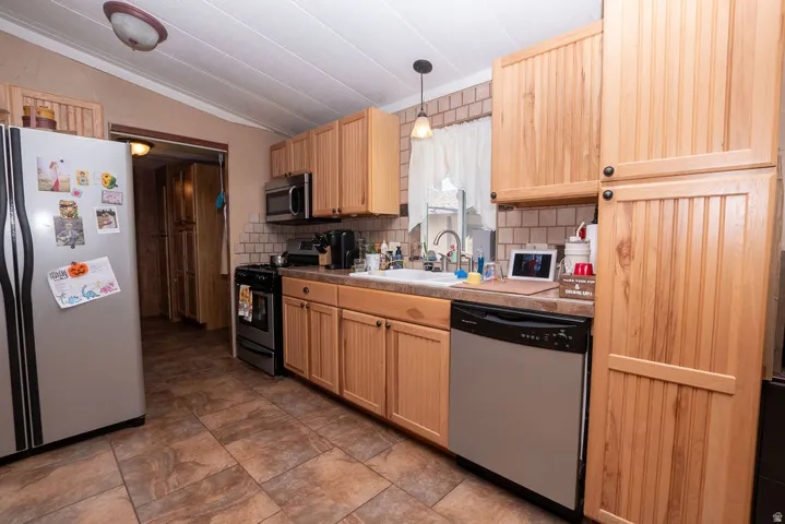 Kitchen featuring wood cabinetry, stainless steel appliances, a tile backsplash, durable tile flooring, and a window above the sink