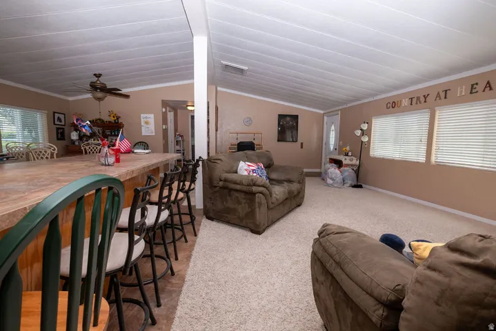 Open-concept living space featuring vaulted ceilings, light-tone carpeting, and multiple windows with horizontal blinds