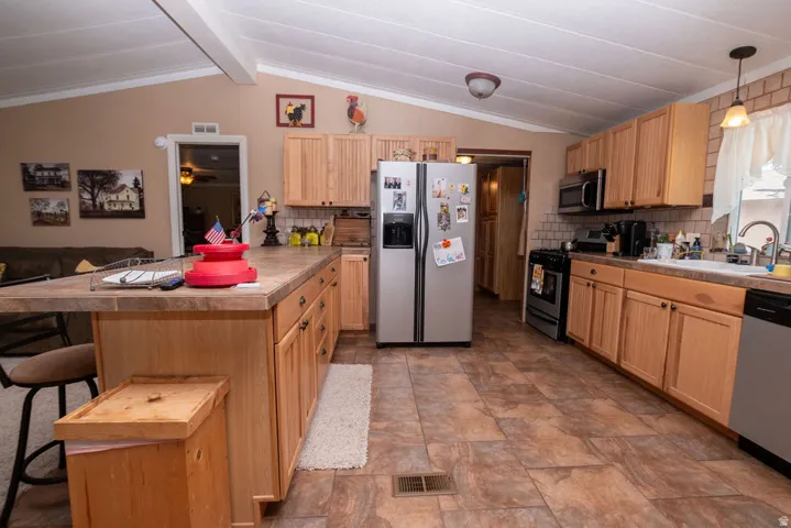 Spacious kitchen featuring light wood-finish cabinetry, a central island with an extended countertop, and a tiled backsplash
