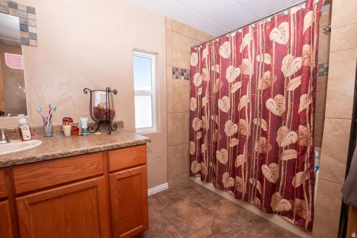 Bathroom featuring wood cabinetry, a speckled countertop with an integrated sink, tile flooring, and a tiled shower surround with decorative accent tiles