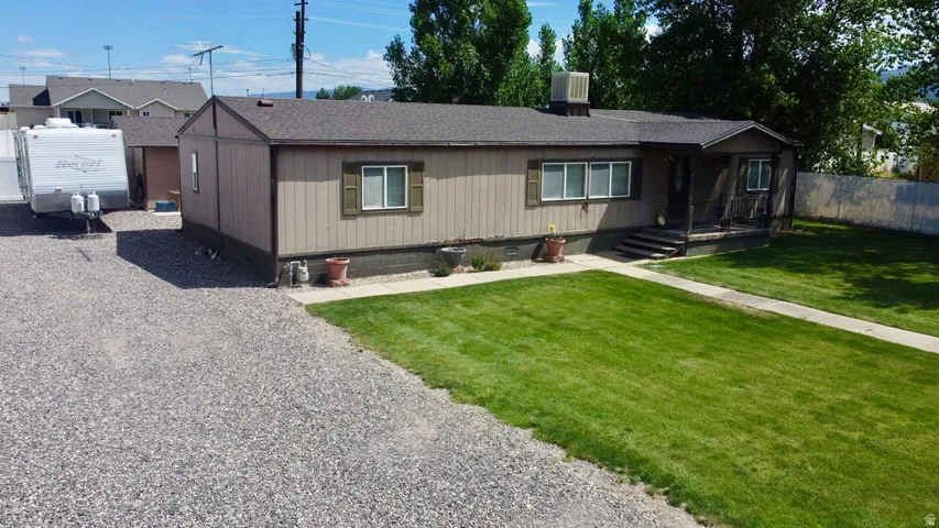 Single-level residence featuring a gravel driveway, a grassy front yard, and a covered porch entry