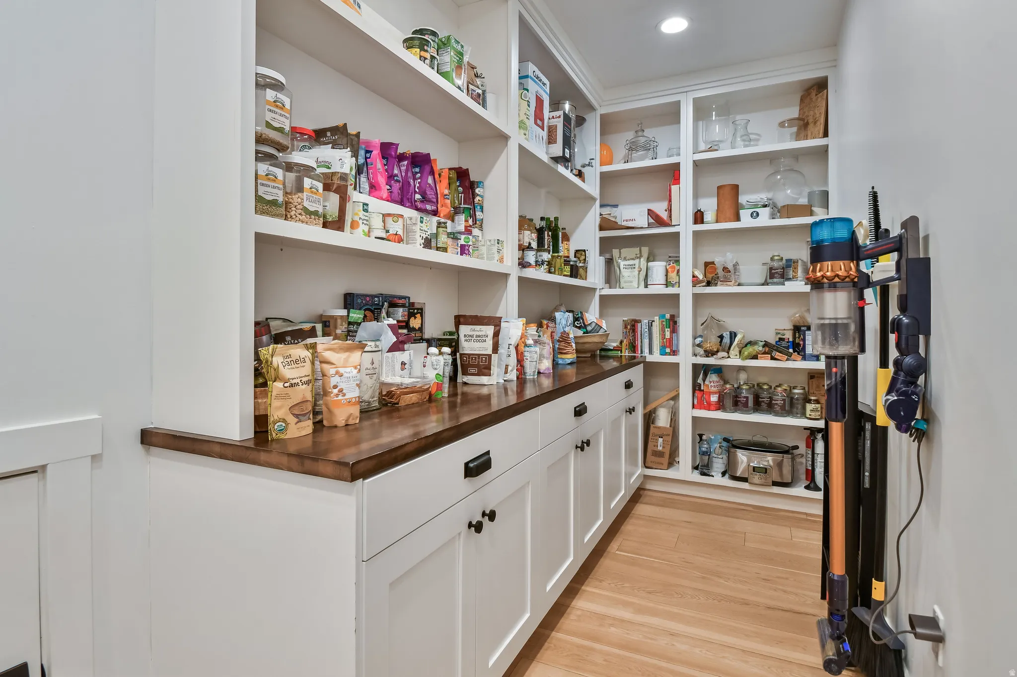 Pantry featuring extensive built-in shelving, white cabinetry with dark hardware, and wood-finish flooring