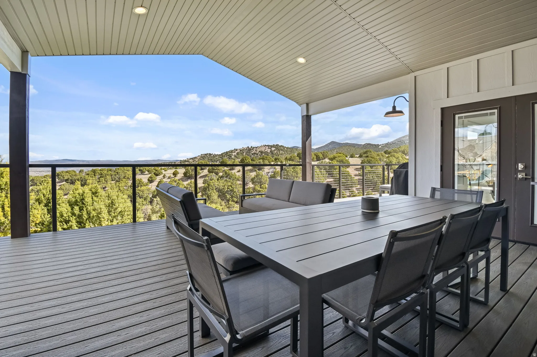 Covered outdoor deck featuring composite decking, a clear railing system, recessed lighting, and a barn-style sconce