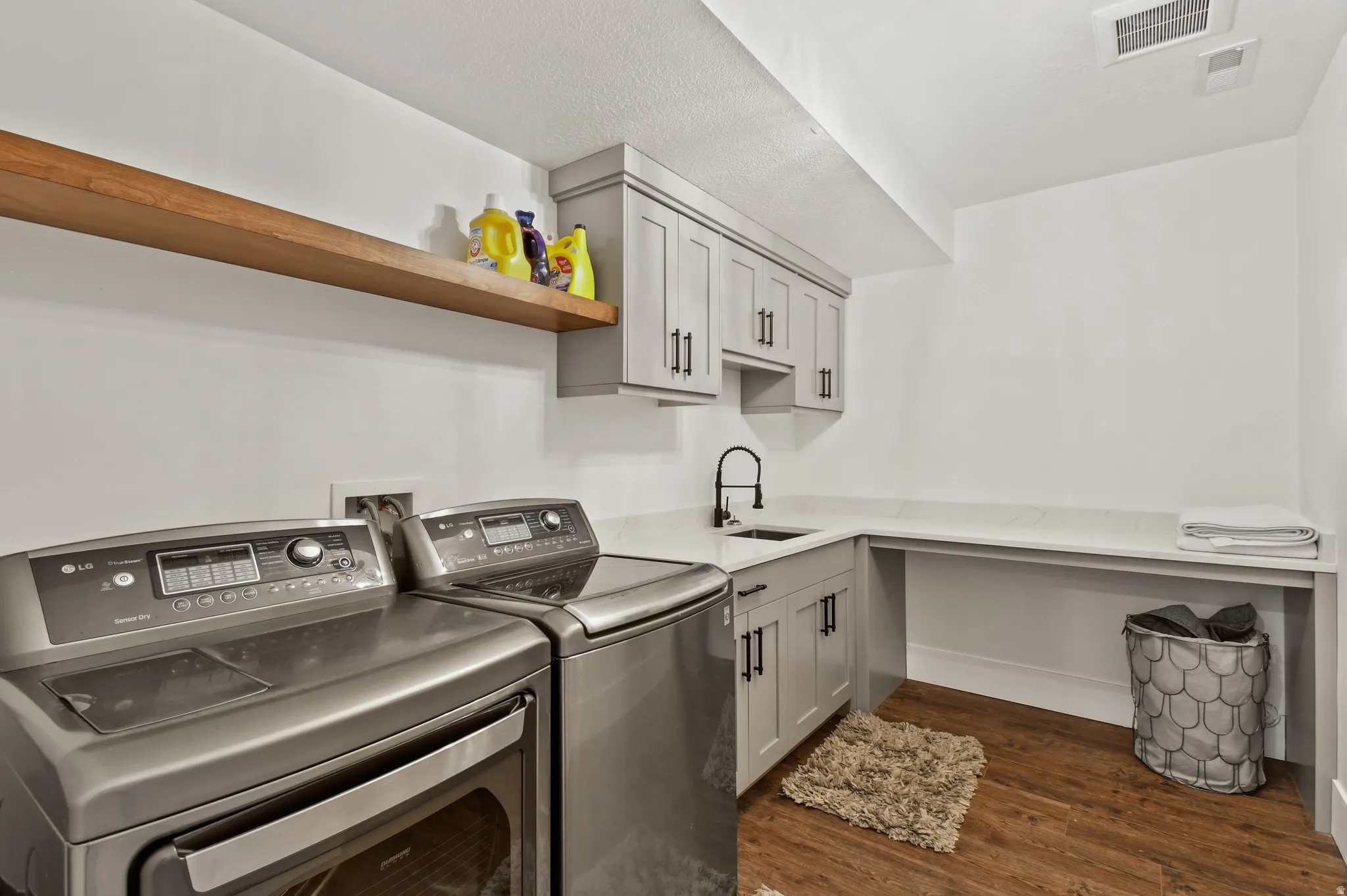downstairs dedicated laundry area featuring wood-finish flooring, light grey cabinetry with matte black hardware, a black-finish faucet, and a light-toned countertop with integrated sink