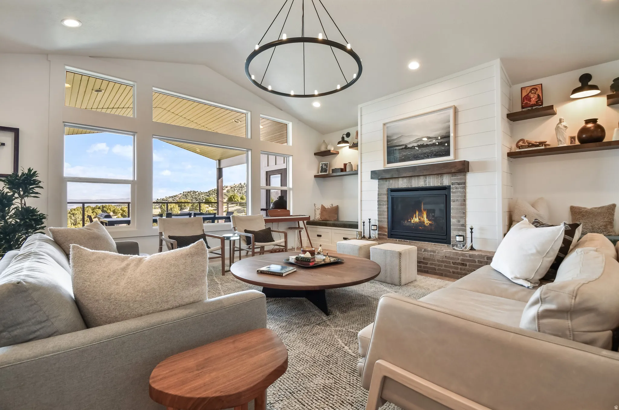 Spacious living area featuring a vaulted ceiling and a prominent fireplace with a brick surround and wood-beam mantel