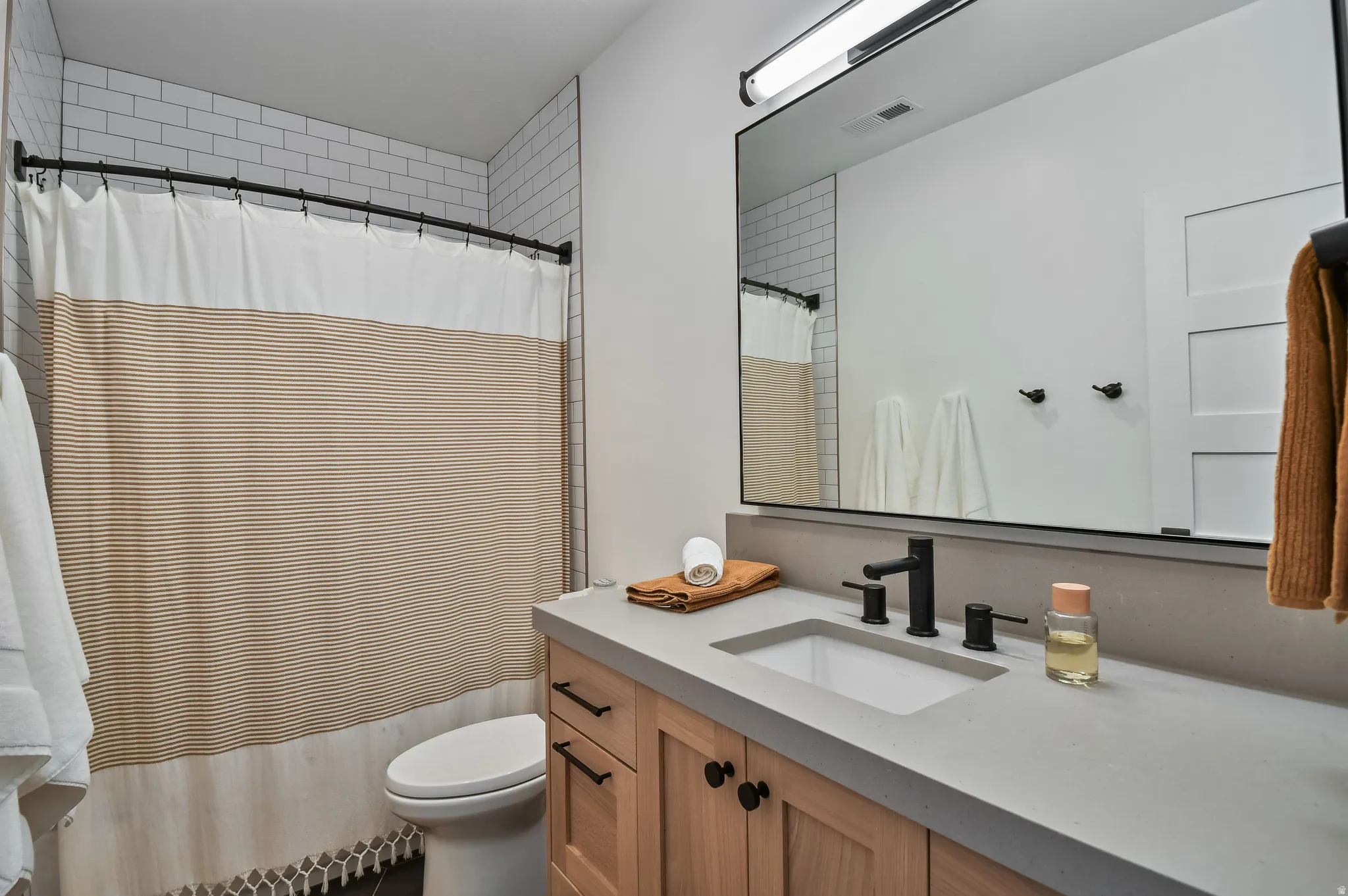 Bathroom featuring a light wood vanity with black hardware, an integrated sink, and a light gray countertop