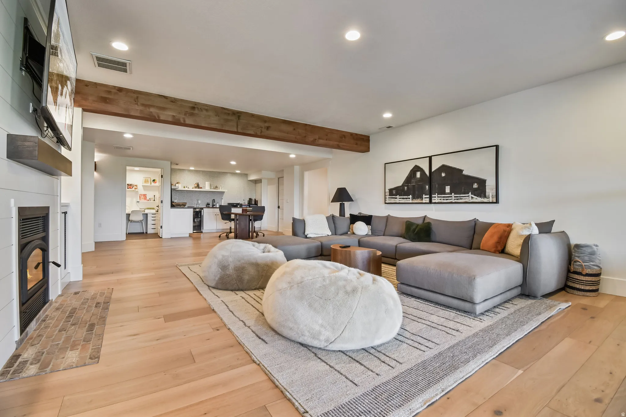 Basement family room with spacious living area featuring exposed wood beam, recessed lighting, wood-finish flooring, a shiplap fireplace with a dark metal insert, and rear-yard access via glass-paned double doors