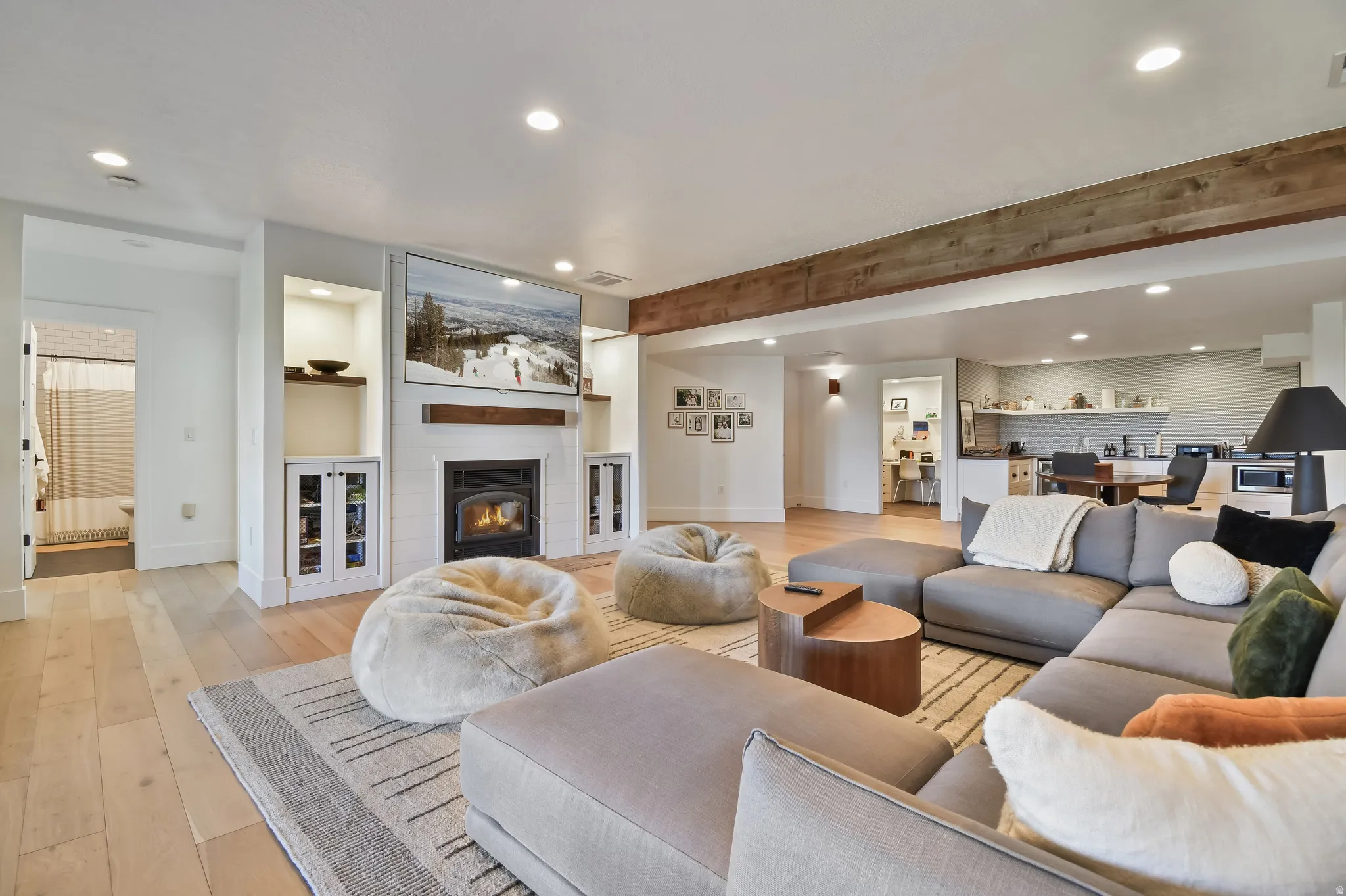 Basement family room with spacious living area featuring exposed wood beam, recessed lighting, wood-finish flooring, a shiplap fireplace with a dark metal insert, and rear-yard access via glass-paned double doors