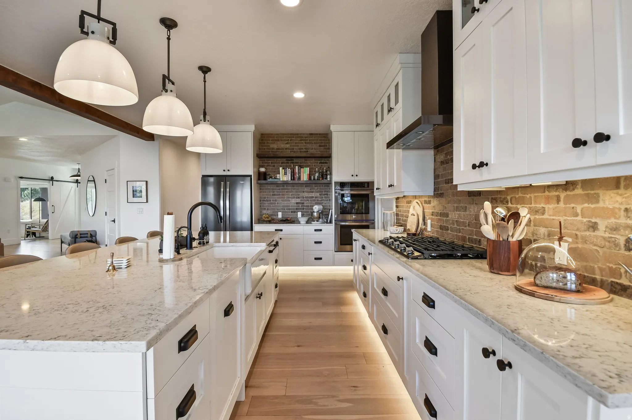 Gourmet kitchen featuring a substantial island with an undermount sink, white cabinetry with matte black hardware, light-toned countertops, a brick backsplash, and wood-finish flooring