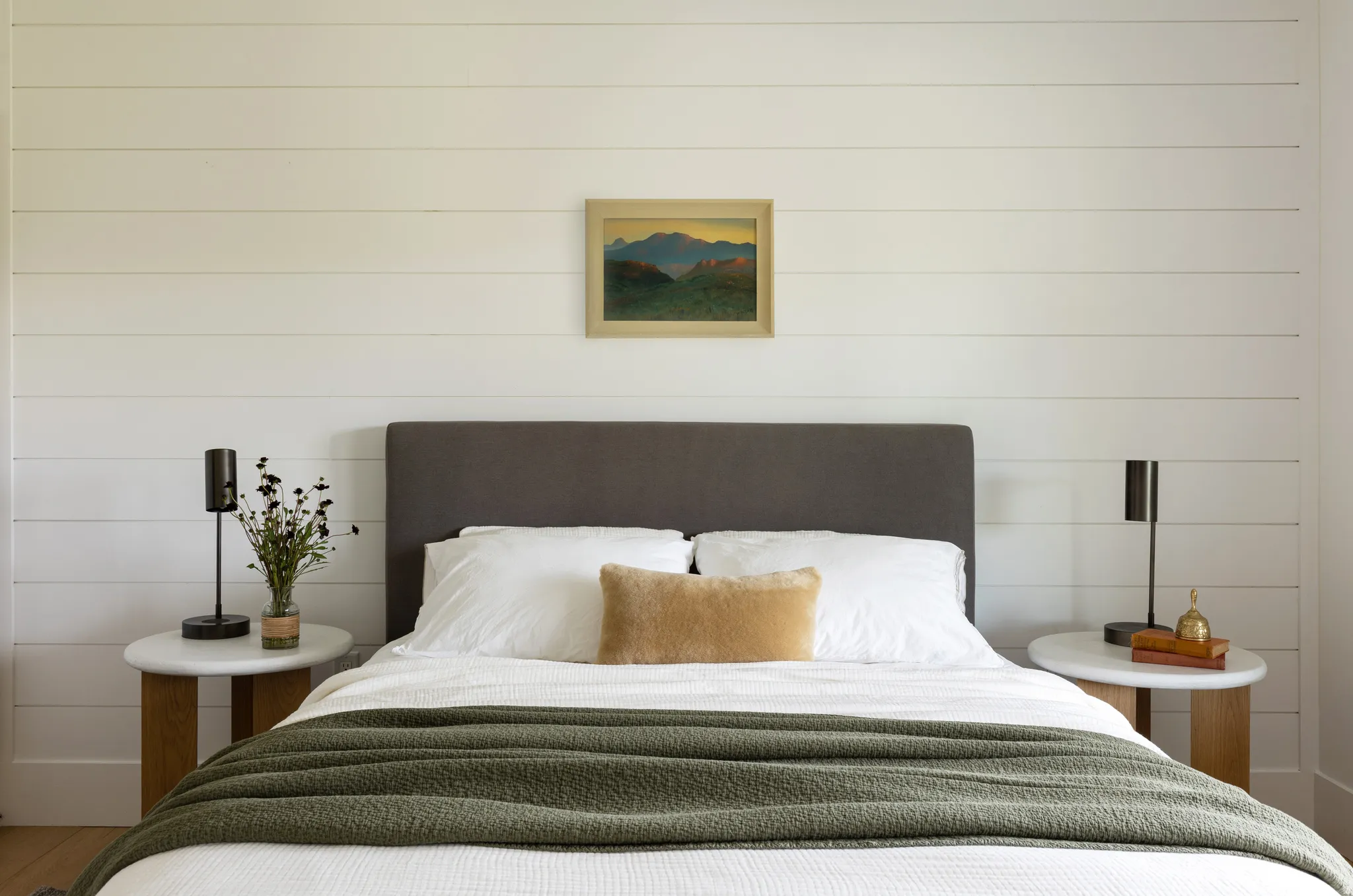 Bedroom featuring shiplap wall treatment, a dark upholstered headboard, and two round side tables with wood bases