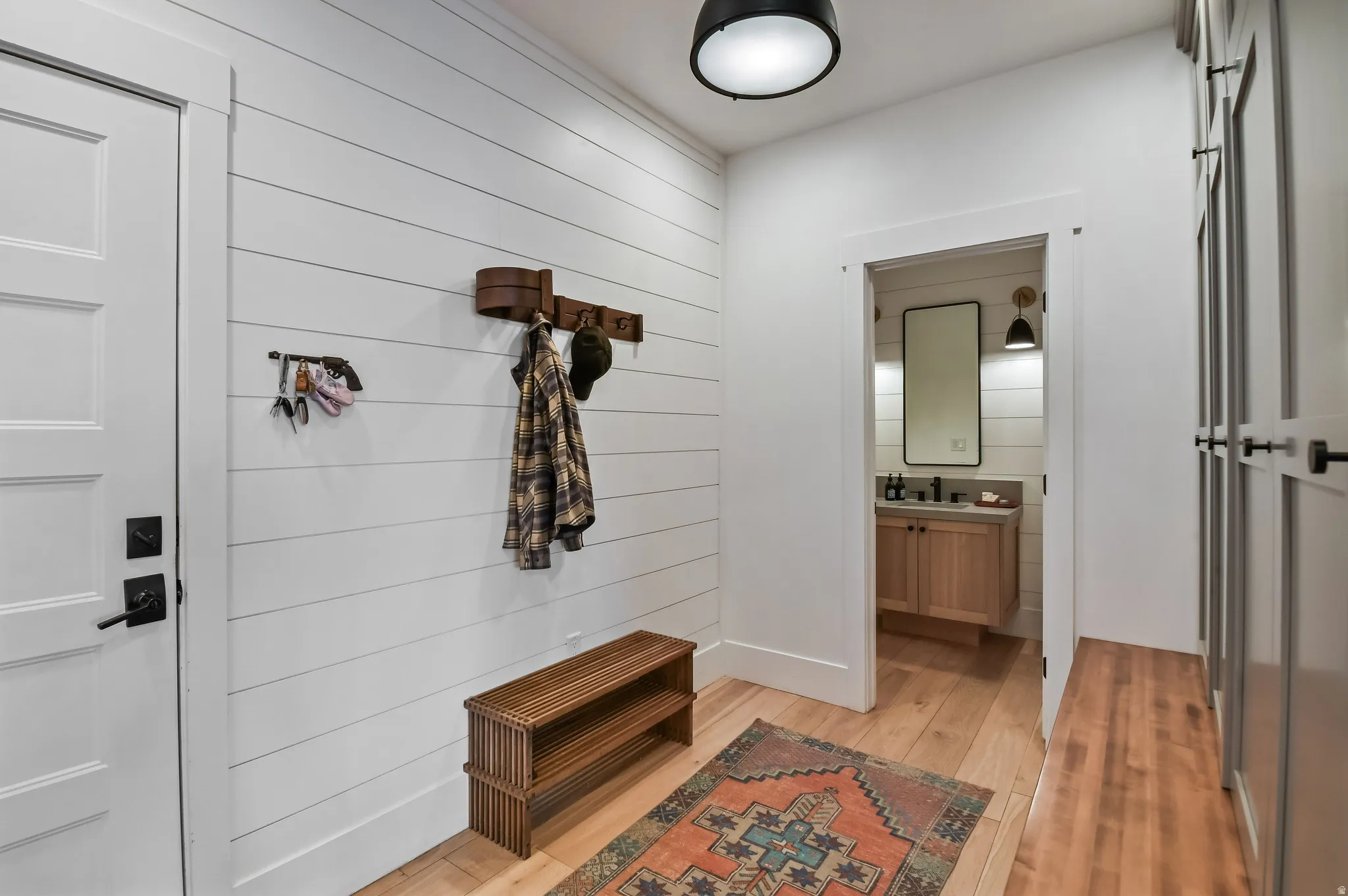 Entryway featuring light wood-finish flooring, white shiplap walls, a solid panel interior door with matte black hardware, and an open doorway to an adjacent space with a vanity