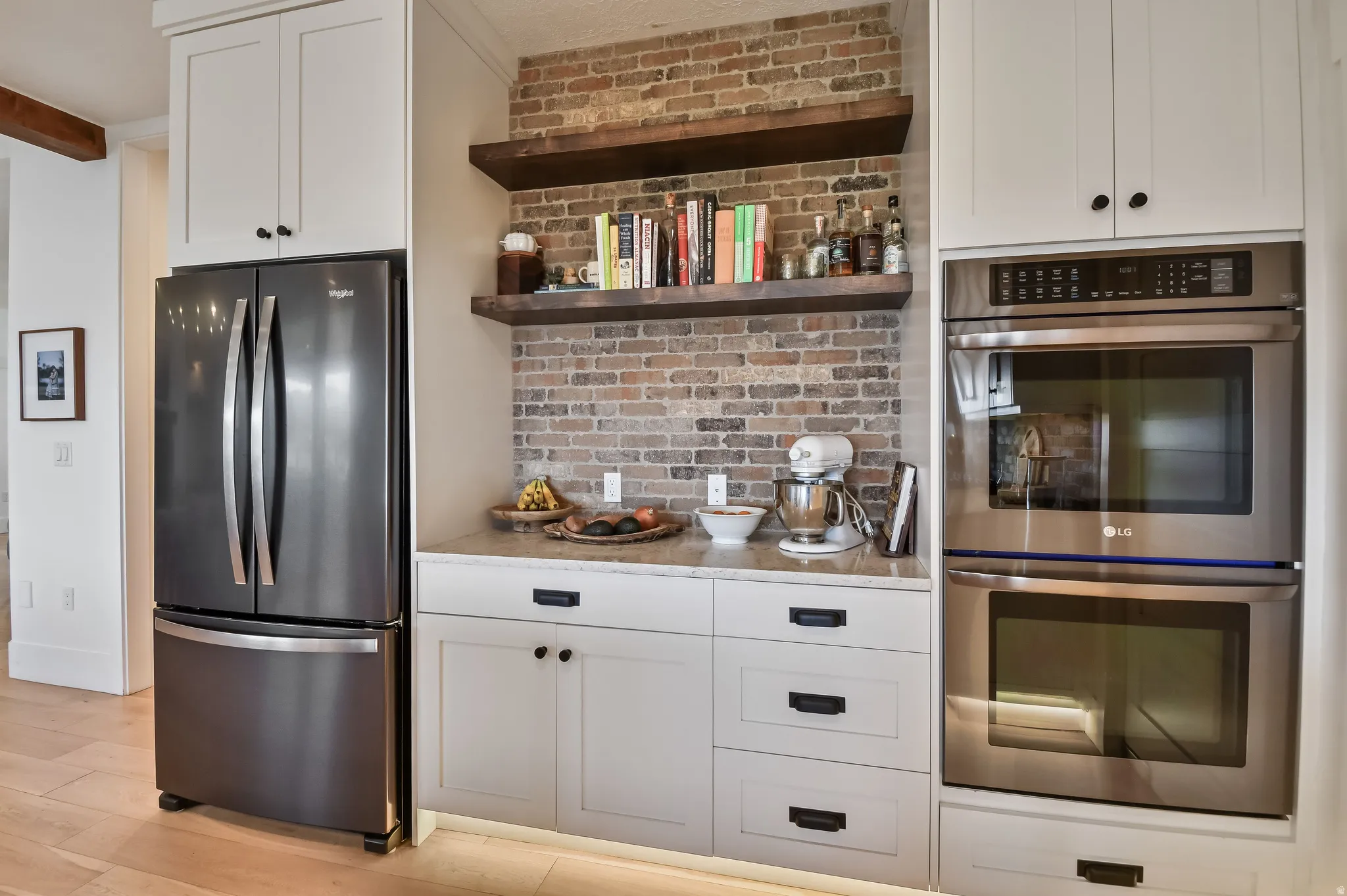 Kitchen featuring white cabinetry, light-colored countertops, a brick-textured backsplash, and dark wood floating shelves