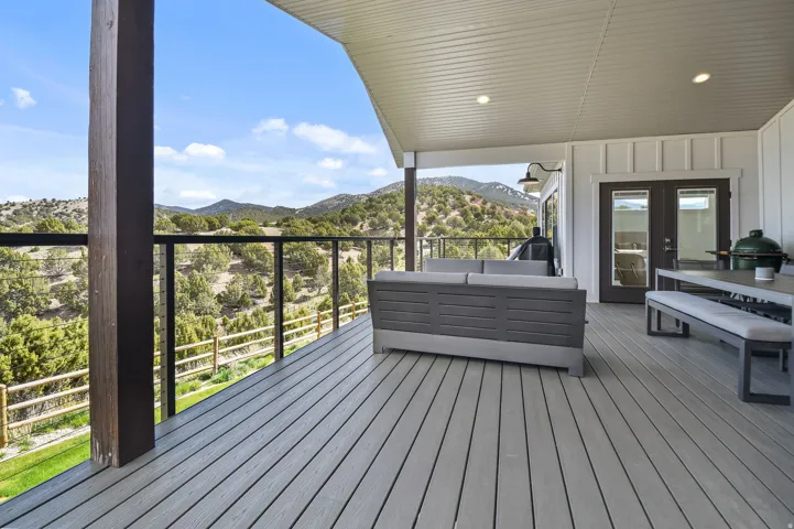 Expansive covered deck featuring composite decking, glass panel railings, recessed lighting, and a board and batten exterior wall