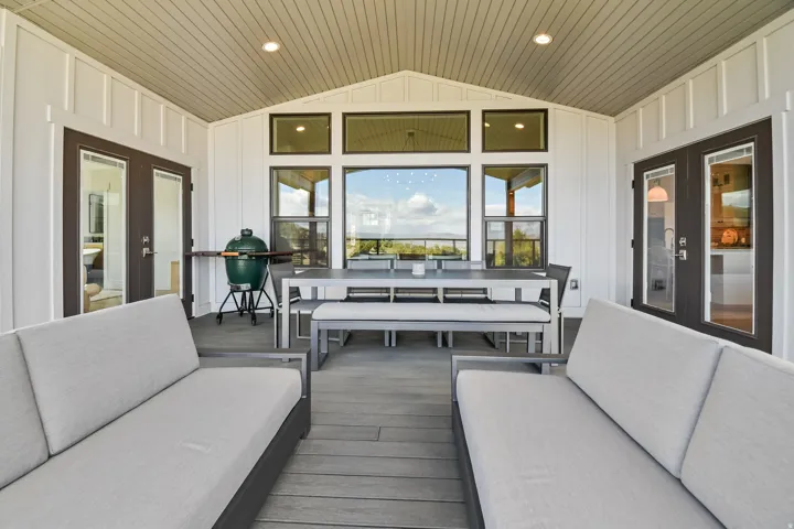 Covered outdoor space featuring a vaulted ceiling with recessed lighting, board and batten siding, large framed windows, and two sets of glass-paneled double doors
