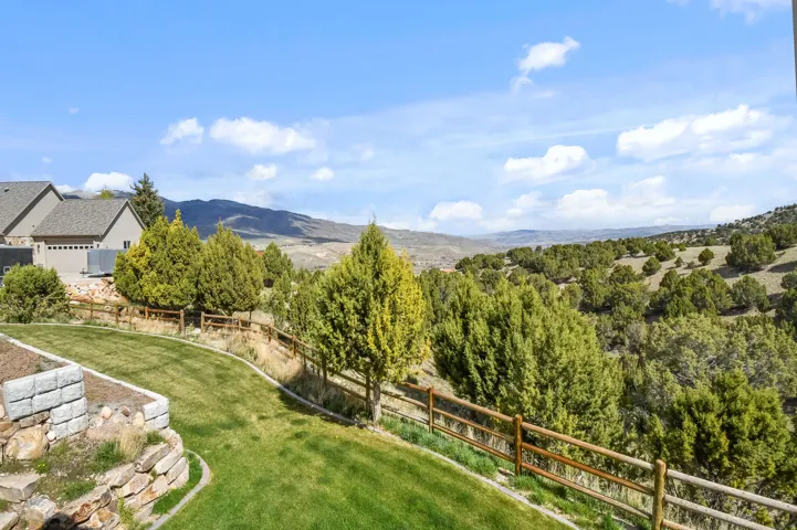 Expansive backyard featuring a manicured lawn, tiered landscaping with stone retaining walls, and a rustic split-rail fence bordering natural terrain
