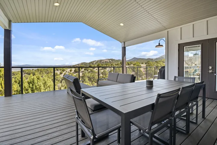 Covered outdoor deck featuring composite decking, a clear railing system, recessed lighting, and a barn-style sconce