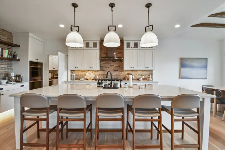 Spacious kitchen island with seating for five, complemented by white cabinetry, brick accent walls, wood-finish flooring, and integrated lighting