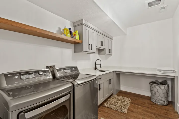 downstairs dedicated laundry area featuring wood-finish flooring, light grey cabinetry with matte black hardware, a black-finish faucet, and a light-toned countertop with integrated sink