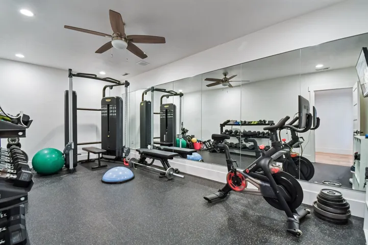 Dedicated fitness space featuring rubber flooring, a full wall of mirrors, and recessed lighting