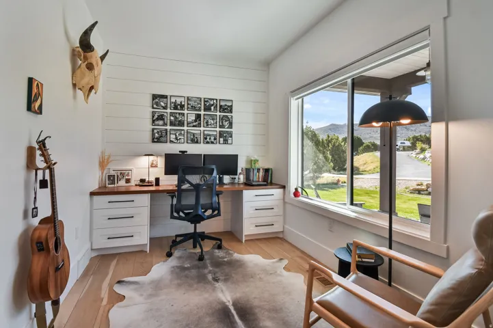 Dedicated workspace featuring a large window, wood-finish flooring, a built-in desk with white cabinetry.