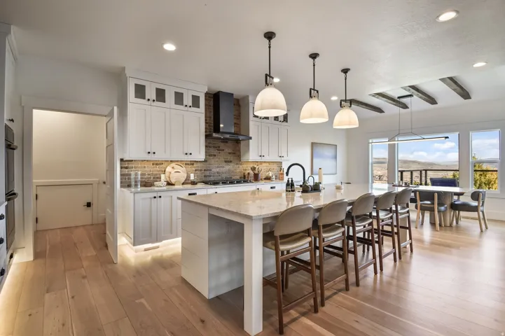 Open-concept kitchen featuring light wood-finish flooring, a large island with seating, white cabinetry, a brick-patterned backsplash, and recessed lighting