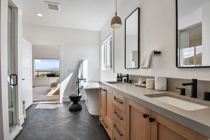 Primary bathroom featuring a dual vanity with light wood cabinetry, stone-finish countertops, and rectangular undermount sinks