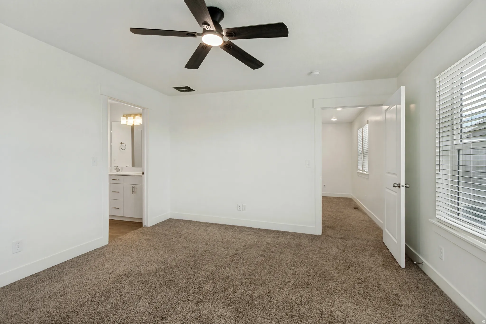 Spacious master suite featuring multiple windows, a ceiling fan with integrated lighting, and a white paneled door