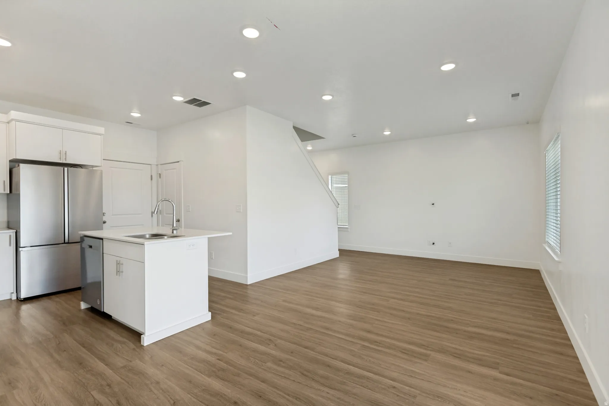 Open-concept living area featuring wood-finish flooring, white walls, recessed lighting, and a quartz kitchen island