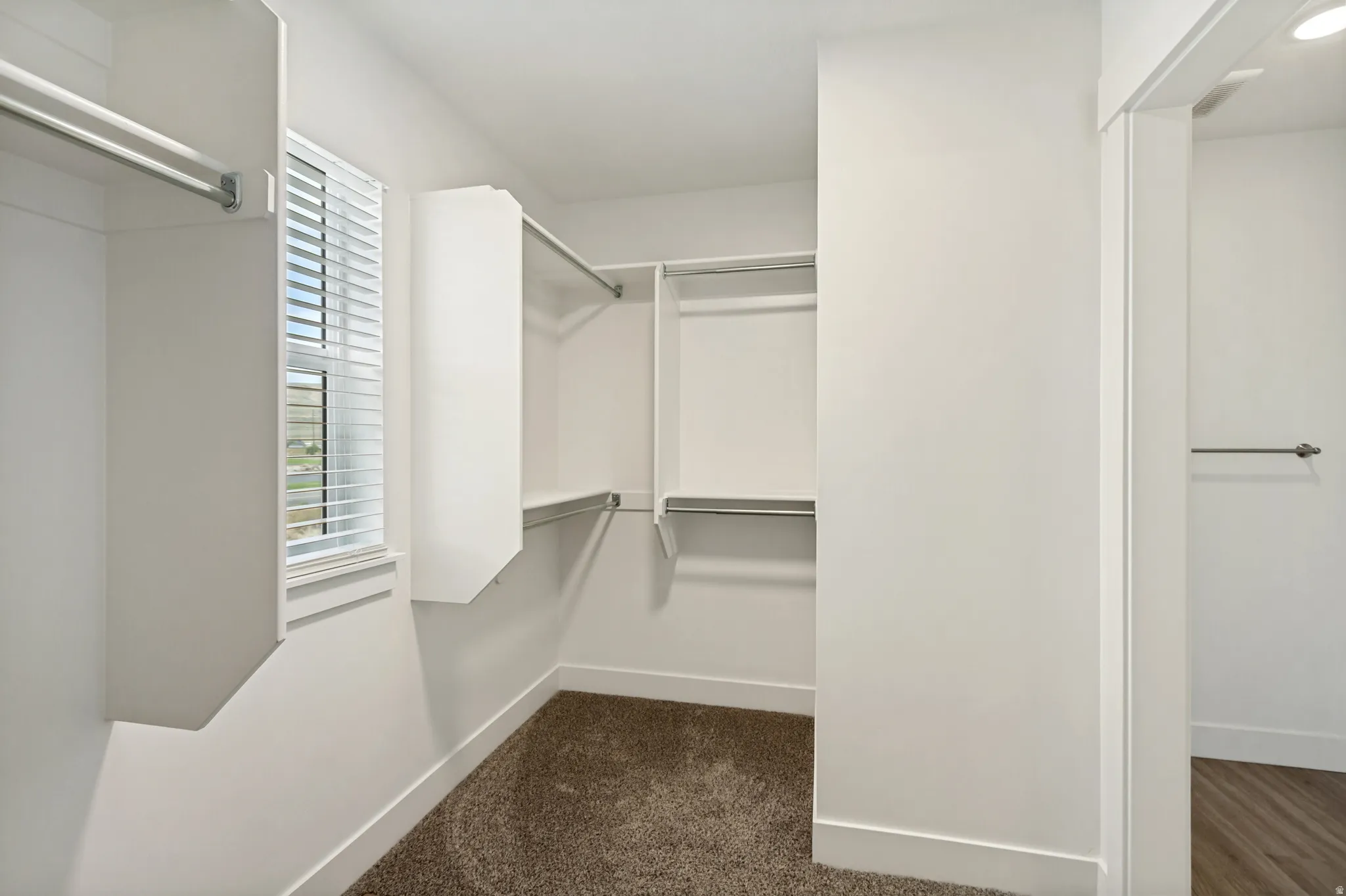 Walk-in closet featuring white built-in shelving, hanging rods, and a window with blinds