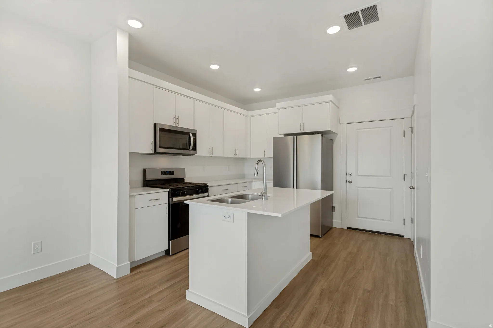 Modern kitchen featuring an quartz island with a double basin sink, white cabinetry, integrated stainless steel microwave, gas range, and laminate flooring
