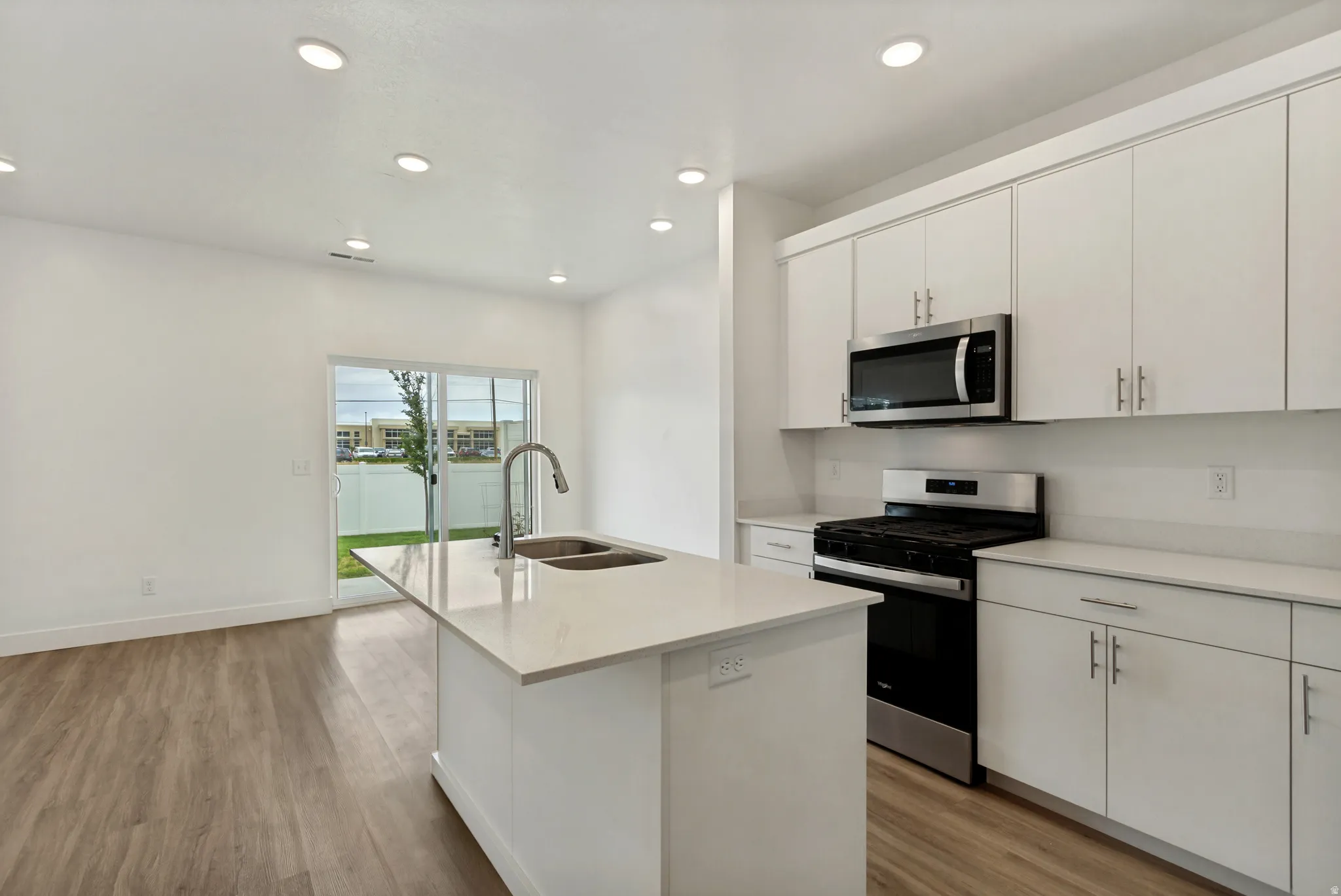 Modern kitchen featuring an quartz island with a double basin sink, white cabinetry, integrated stainless steel microwave, gas range, and laminate flooring