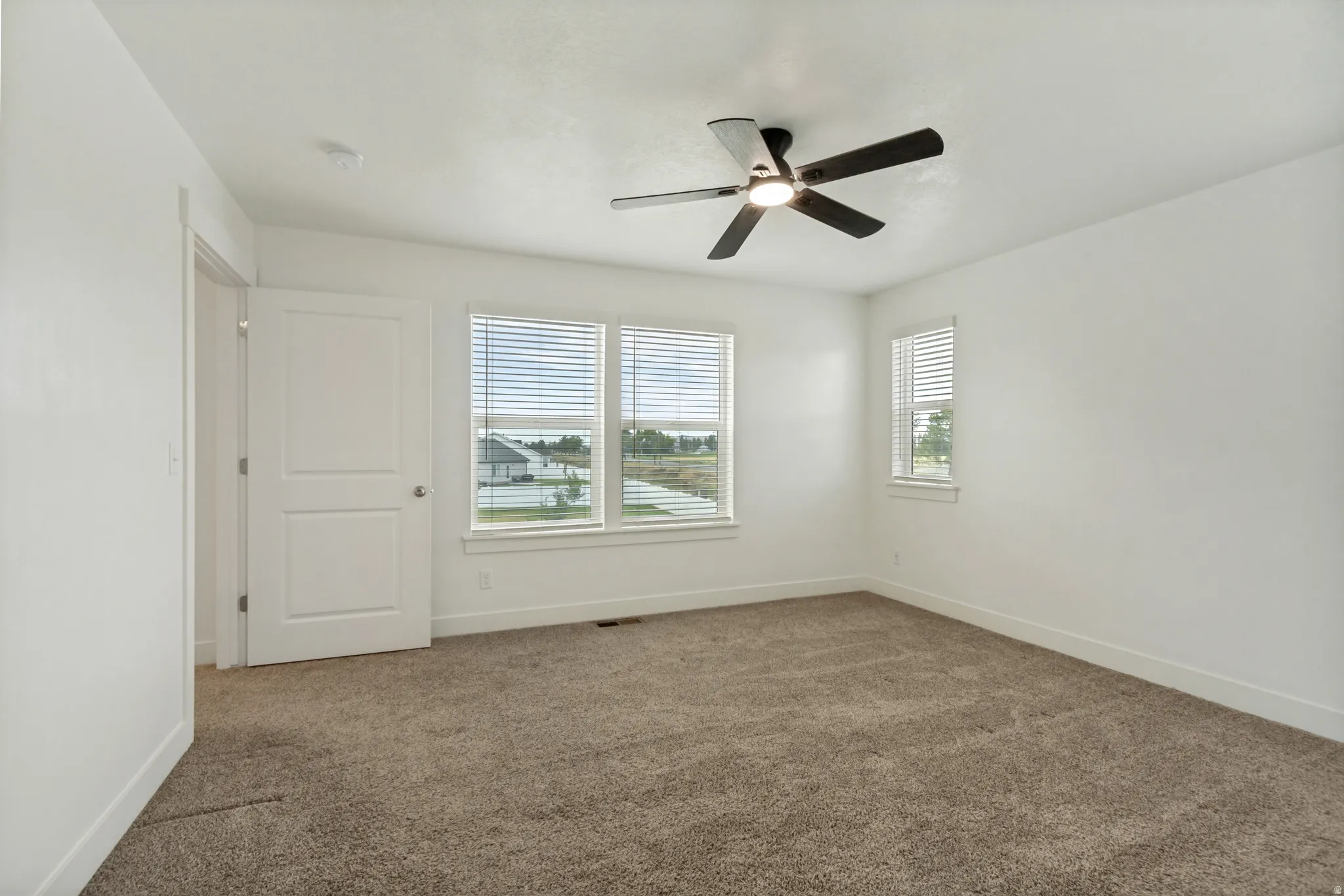 Spacious master suite featuring multiple windows, a ceiling fan with integrated lighting, and a white paneled door