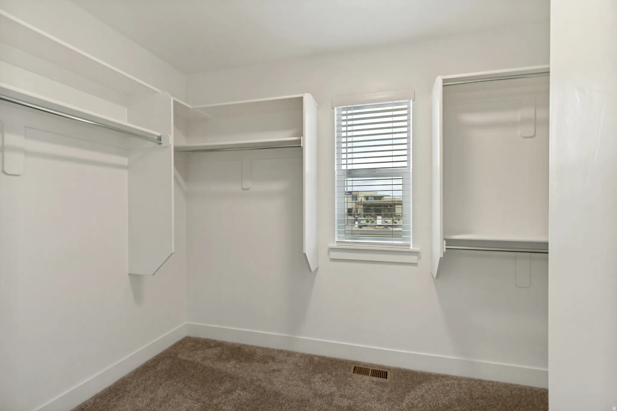 Walk-in closet featuring white built-in shelving, hanging rods, and a window with blinds