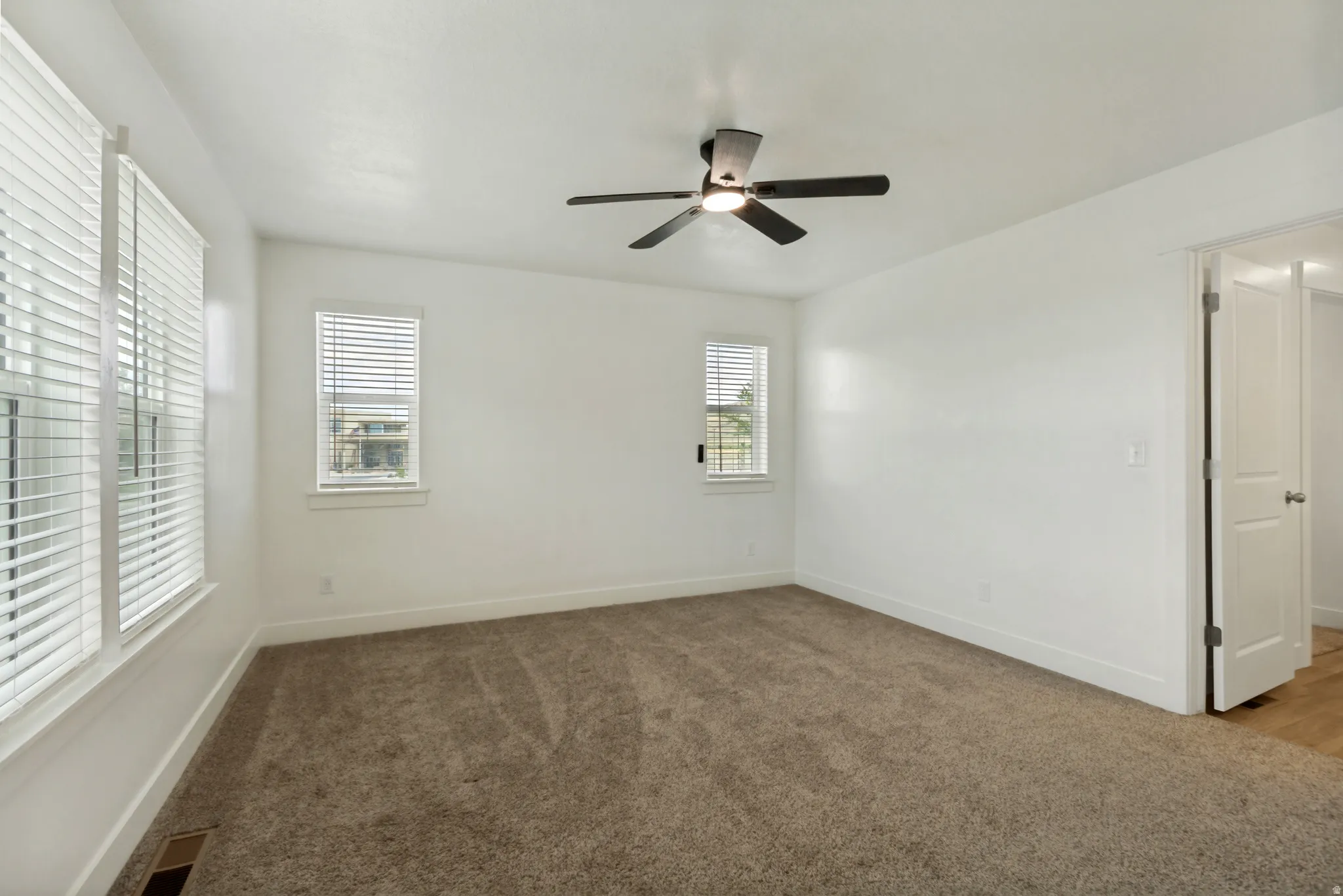 Spacious master suite featuring multiple windows, a ceiling fan with integrated lighting, and a white paneled door